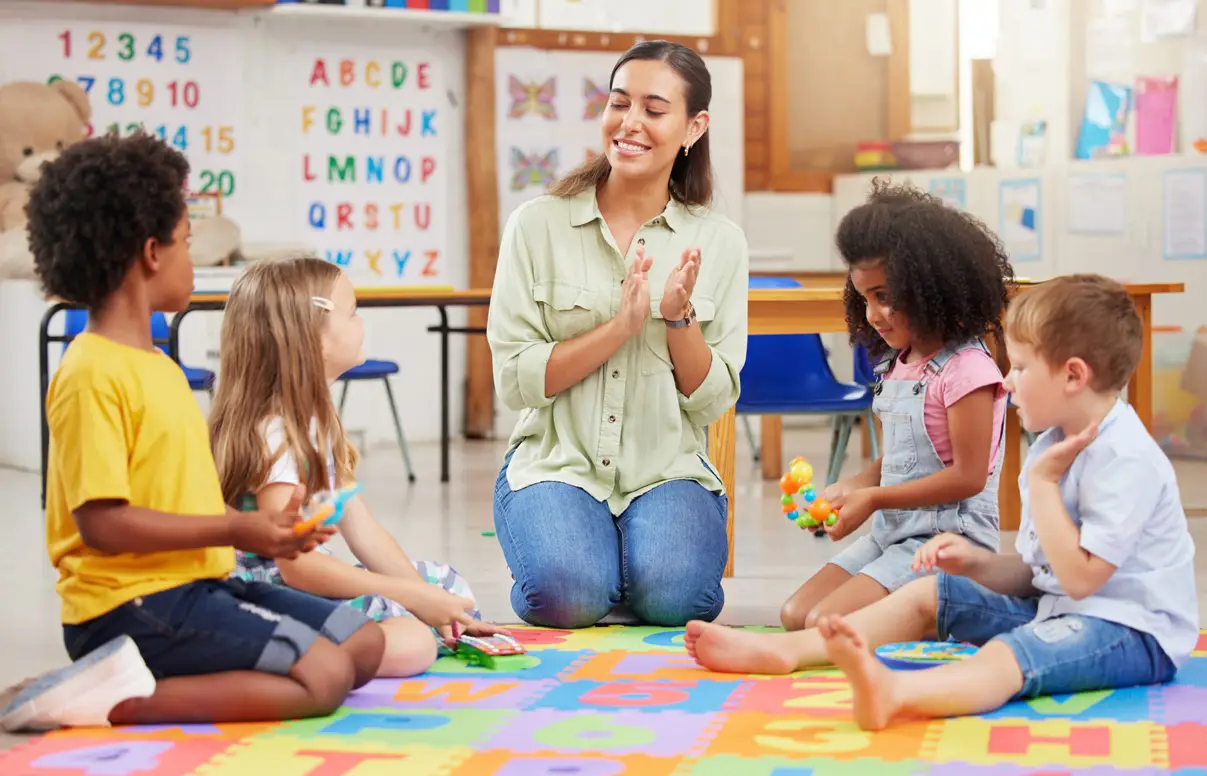 Preschool readiness checklist - a teacher sitting with a small group of preschool children on a play mat