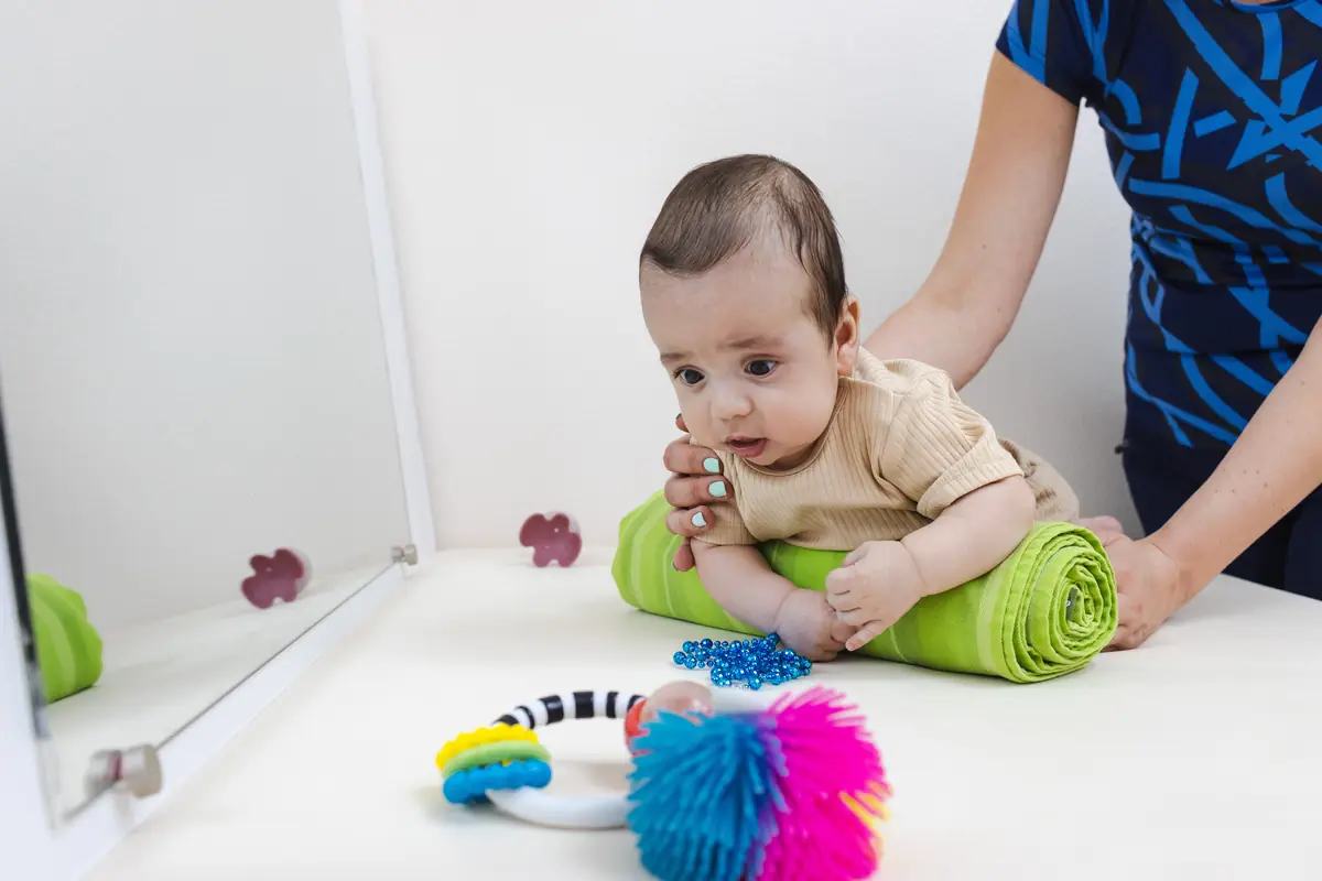 Baby doing tummy time for babies, propped on a rolled towel with a parent supporting and toys in front