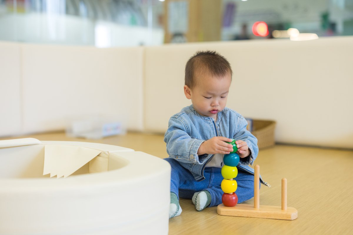 Fine motor skills activities for toddlers - a toddler using a pincer grip to place a wooden ring on a stacking toy