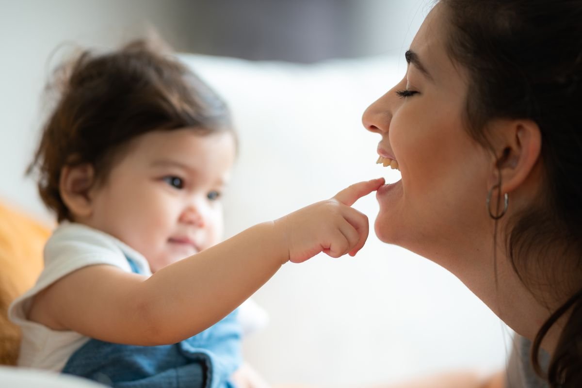 Speech delay in toddlers - a toddler touching her mother's lips as they laugh together, curious about how sounds and words are made